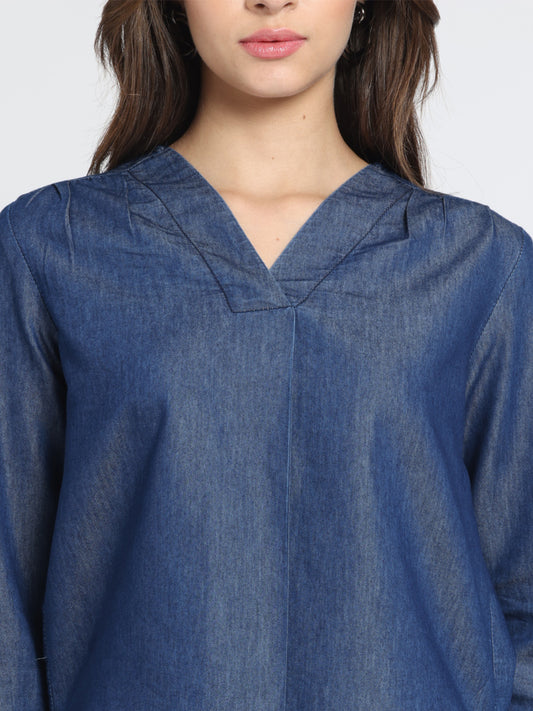 Close-up V-neckline and front pleat detail on blue denim top, showing gathers on shoulder and soft fabric