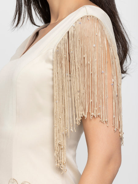 Detailed close-up of floral sequin embroidered patch and fringed sleeve on beige satin sheath dress