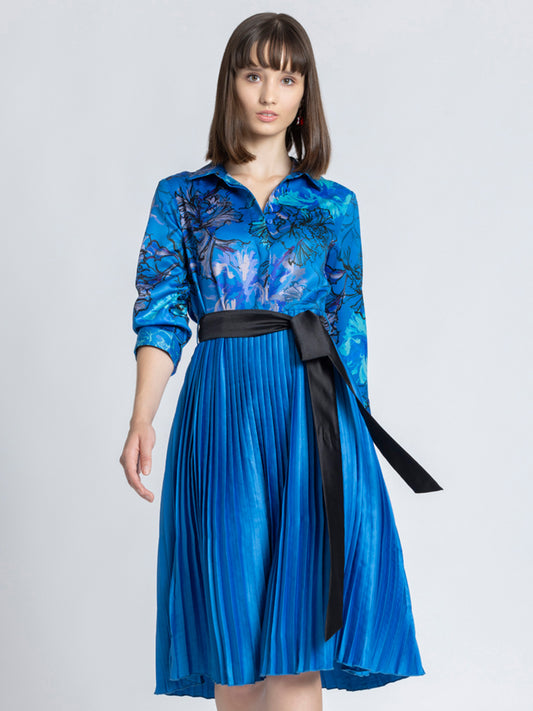 Model wearing blue floral print Olga Dress with shirt collar long cuff sleeves pleated skirt and belt