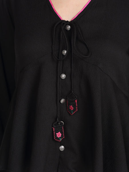 Detailed view of button front and embroidered tassels on black crinkled crepe peplum top
