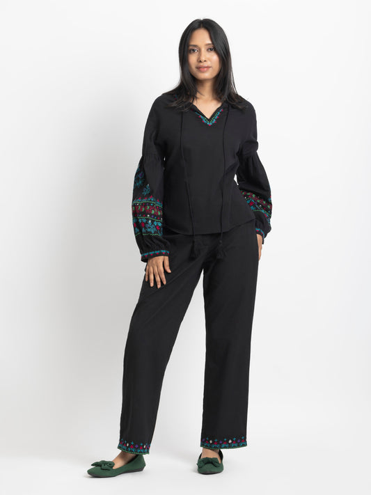 Model standing with hand in pocket wearing black embroidered Shiloh Co-ord Set with V-neckline and elasticated sleeves