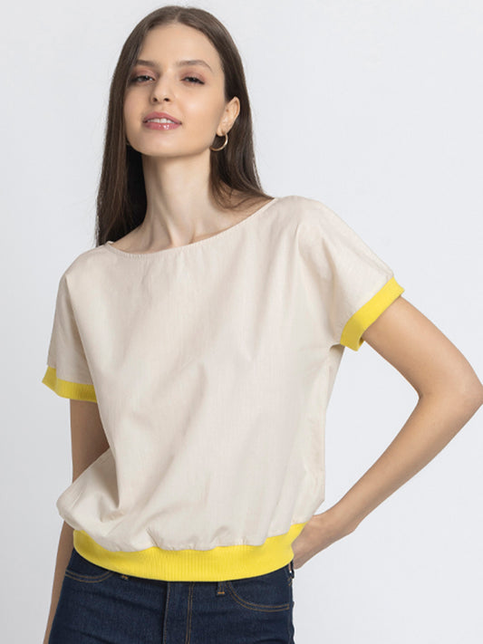 Model with hand on hip wearing beige Sullivan Top with boat neck short drop shoulder sleeves and ribbed hem